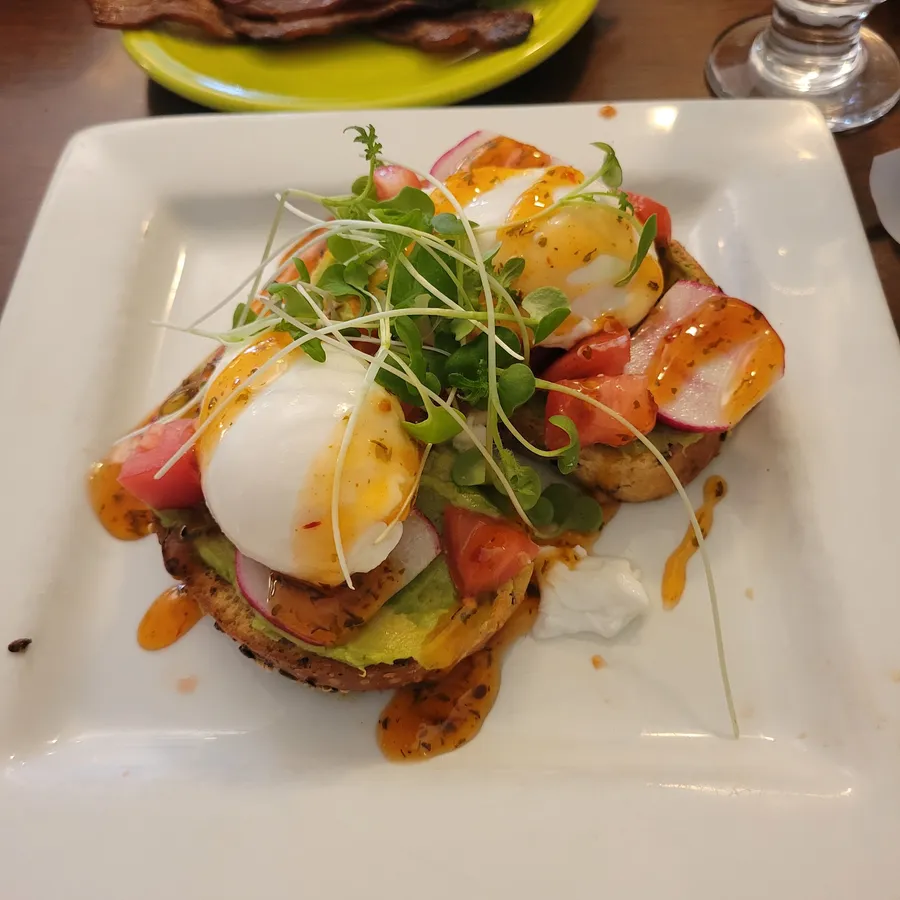 Avocado toast with two poached eggs, tomato, radish and micro greens