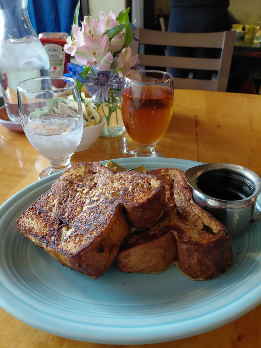Thick cinnamon French toast with syrup, iced tea and fresh flowers on the table