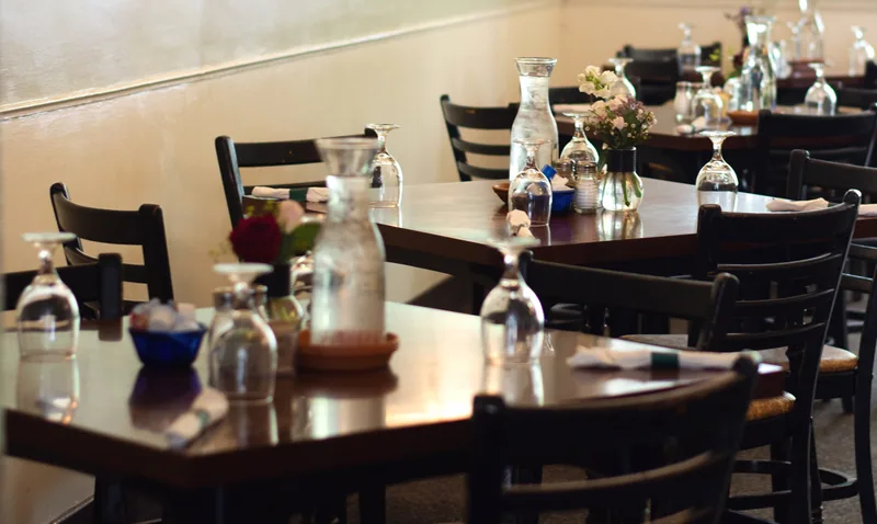 Dark wood tables and black ladder-back chairs with water carafes and fresh flowers.