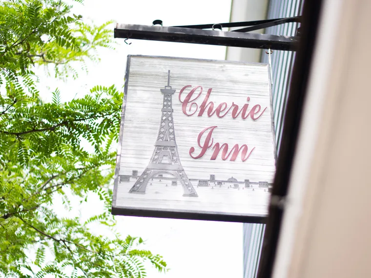 The hanging Cherie Inn sign — a pewter Eiffel Tower and rose script on whitewashed wood.